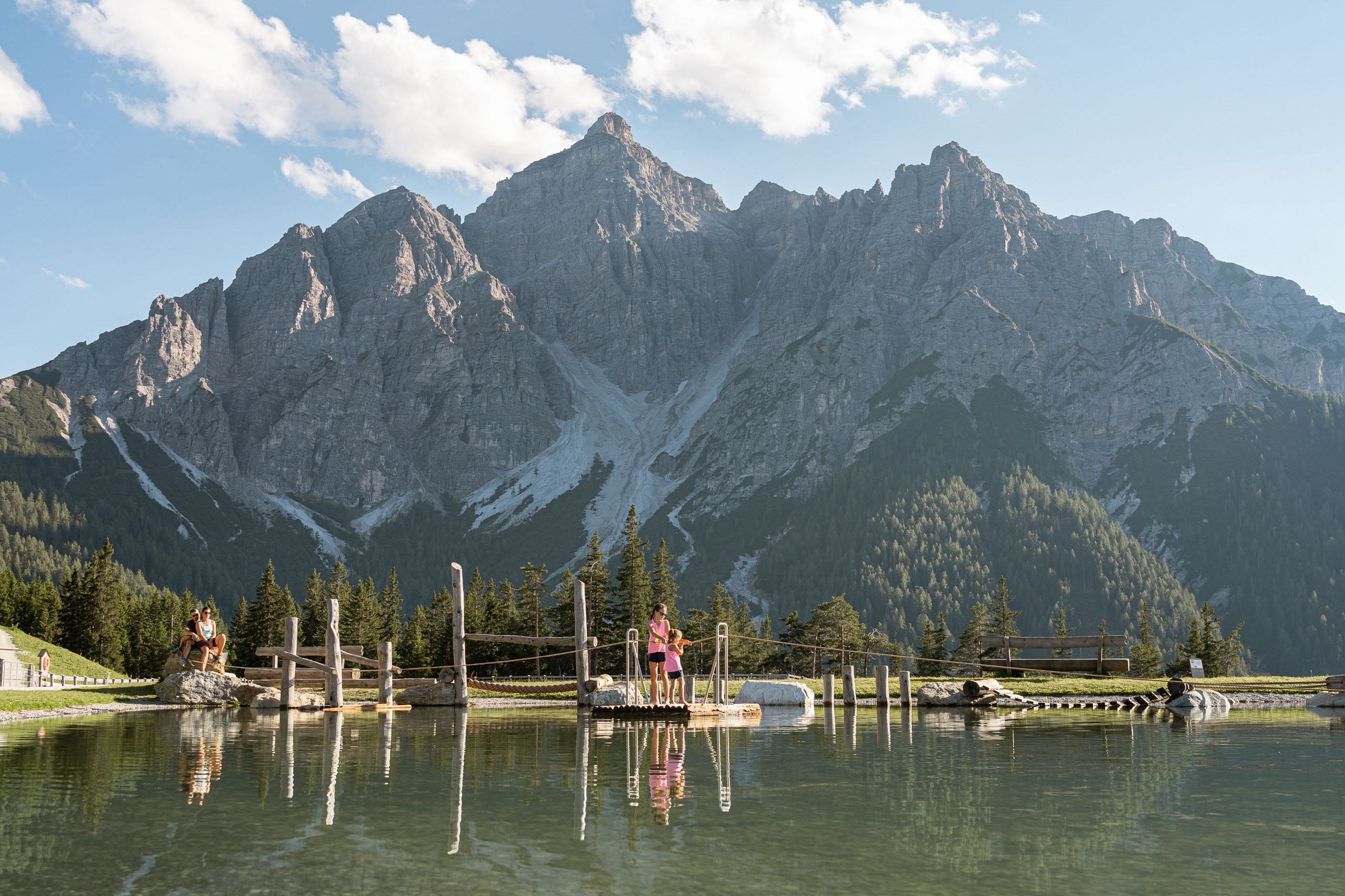 Zwei Kinder ziehen sich auf einem Floß der Schnur entlang über den See der Serlesbahnen Mieders